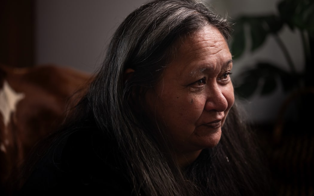 Joyce Harris, photograhed during an interview with RNZ in her living room. She sits in an armchair, holding a blue bandana tightly in her hands.