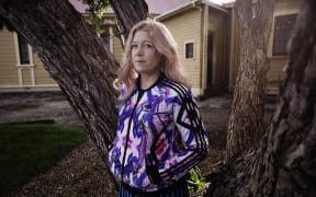 Sarah, subject of Nellie's Baby stands in front of tree outside of Porirua Hospital Museum