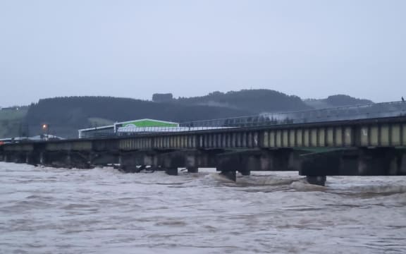 The Mataura River at Gore is flowing swiftly and some debris is caught under a rail bridge.
