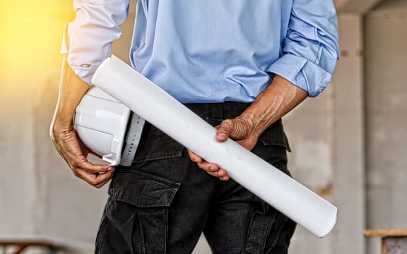 Back view of engineer holding blue print and white helmet