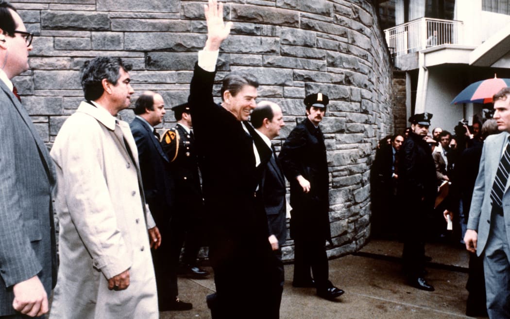 This photo taken by presidential photographer Mike Evens on March 30, 1981 shows President Ronald Reagan waving to the crowd just before the assassination attempt on him, after a conference outside the Hilton Hotel in Washington, D.C.. Reagan was hit by one of six shots fired by John Hinckley, who also seriously injured press secretary James Brady (just behind the car).  Reagan was hit in the chest and was hospitalized for 12 days. Hinckley was aquitted 21 June 1982 after a jury found him mentally unstable. (Photo by MIKE EVENS / CONSOLIDATED NEWS PICTURES / AFP)