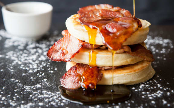 Female hand pouring maple syrup over breakfast bacon crumpet on slate