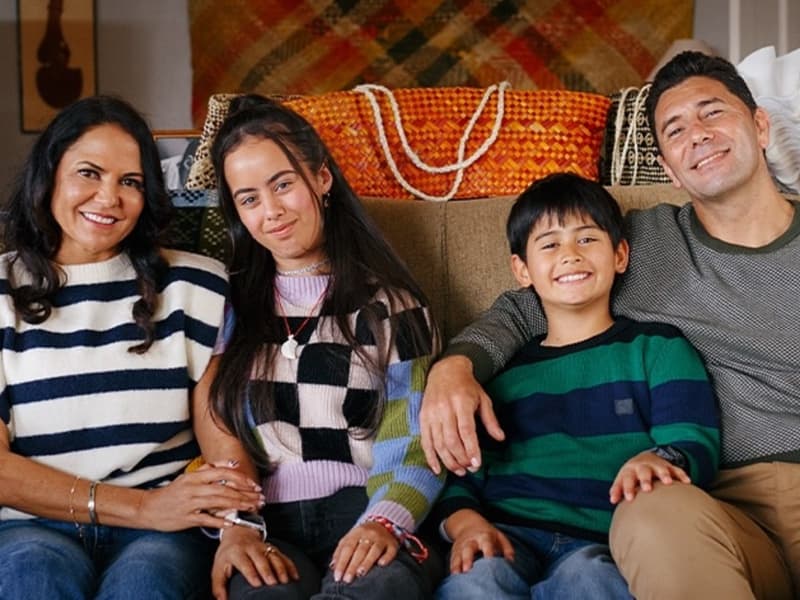 A Maori family of four face the camera with arms around each other.