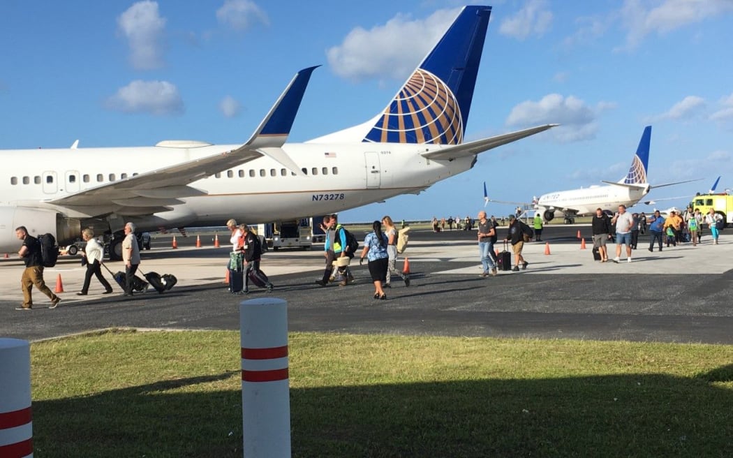 Passengers and flight crew who slept on a grounded United Airlines plane (rear) because of a Marshall Islands Covid-19 ban on incoming travelers deplane and walk to a rescue flight that arrived
Majuro shortly before 8am to collect the 124 passengers and flight crew.