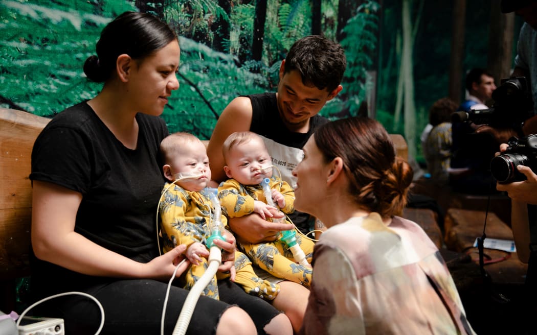 New parents Michaela Jane Beach and Vincent Moeke holding Sarge (left) and Bycie Beach-Moeke (right), alongside Prime Minister Jacinda Ardern