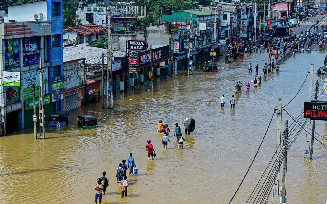 People wade through a flooded street after heavy rainfall in Wellampitiya on the outskirts of Colombo on November 30, 2025.