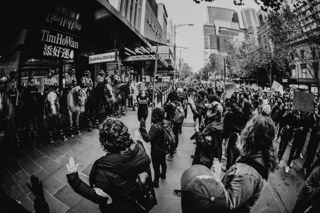 Aboriginal members of the Melbourne Black Lives Matter march stand in between horse-bound police and the rest of the protester with their hands raised.