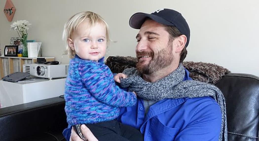 A father in his 30s holds his toddler on his lap