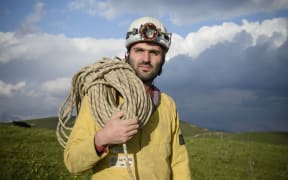 Cave explorer Francisco Sauro wearing a safety helmet with a headlamp. He is carrying a length of rope and is dressed in overalls