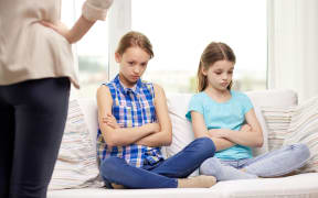 A photo of two girls sitting on the couch and looking chastened after a lecture from their mother