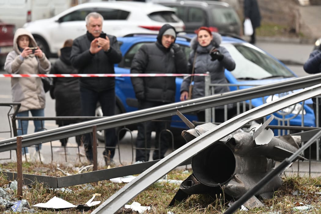 People stand behind the cordoned off area around the remains of a shell in Kyiv on February 24, 2022