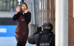 One of the hostages runs towards police from a cafe in the central business district of Sydney on December 15, 2014. Five people ran out of a Sydney cafe where a gunman has taken hostages and displayed an Islamic flag against the window, witnesses and police said December 15, adding that no one has yet been harmed. AFP PHOTO / SAEED KHAN (Photo by SAEED KHAN / AFP)