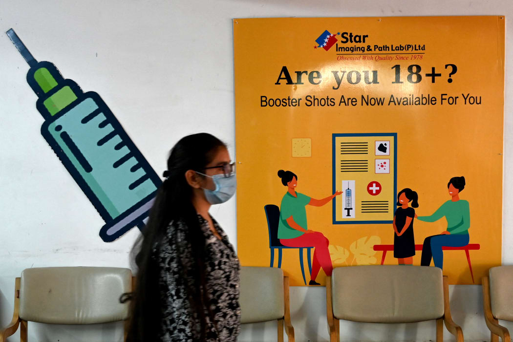 A girl walks past a poster at a vaccination centre in New Delhi on April 10, 2022, after government announced the paid precaution dose against Covid-19 coronavirus to be available for everyone above 18 years of age at private vaccination centres.
