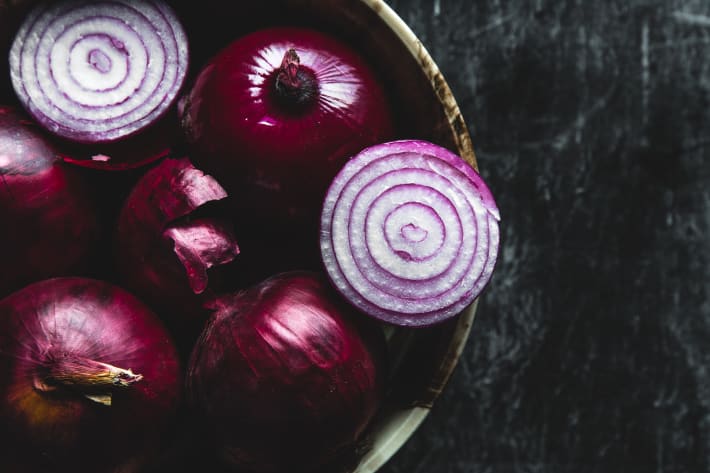 Plate with purple onion. Onions with water droplets. On the table scattered onion husk. Breakfast for a vegetarian