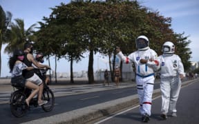 Brazilian accountant Tercio Galdino, 66, gives the thumb up to people riding a motorcycle as he and his wife Alicea Galdino walk along Leme beach in protective suits, in Rio de Janeiro, Brazil on July 12, 2020.