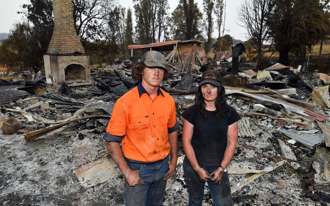 This photo taken on January 8, 2020 shows Kiahan Bellchambers (R) and her brother Jesse Bellchambers posing for a picture amongst the ruins of their house destroyed during bushfires in Batlow, in Australia's New South Wales state. -