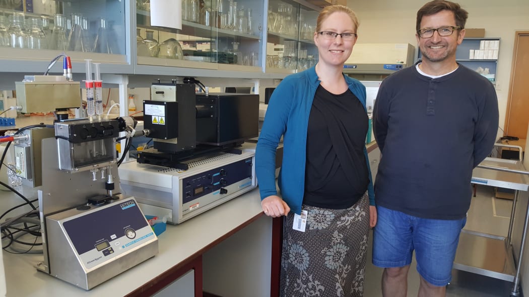 Erica Prentice and Vic Arcus in the lab, standing next to the machine they use to test enzyme reactions at different temperatures.