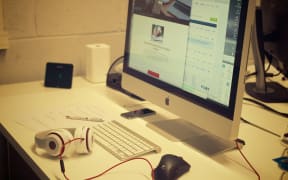 A work station: Apple computer screen, keyboard, headphones, speakers, mouse, pen, paper, desk.