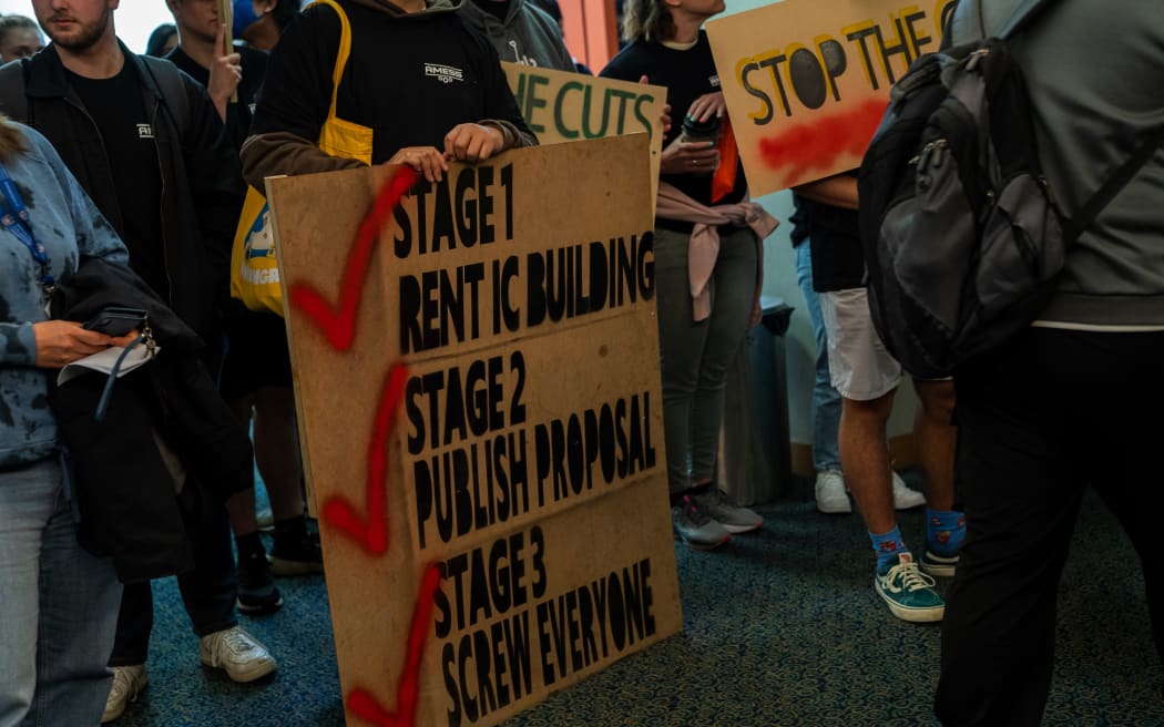 Students holding signs protesting Massey University cuts.