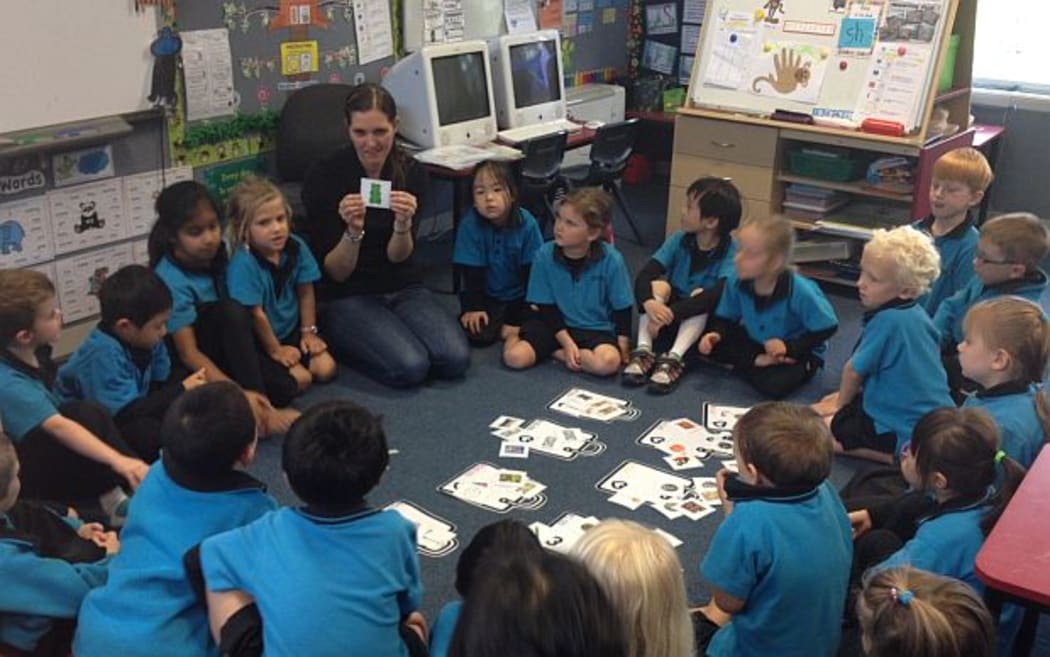 Children sit in a semi circle on the floor listening to their teacher