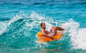 Excited bearded hipster in inflatable ring have fun in beach surf. Funny man riding on tubing in breaking sea waves. Family travel lifestyle, swimming activities. Summer vacation on tropical island.