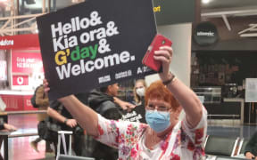 A woman at Auckland Airport holds a welcome sign as flights from Australia are due on the first day that the border has reopened to Australians without a requirement for isolation.
