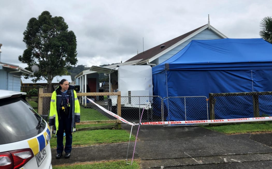 Police are executing a search warrant at a house on Taraire Street in relation to the investigation into the homicide of Linda Woods. At least four officers are guarding the cordoned house and other officers can be seen rummaging through rubbish bins on the property.