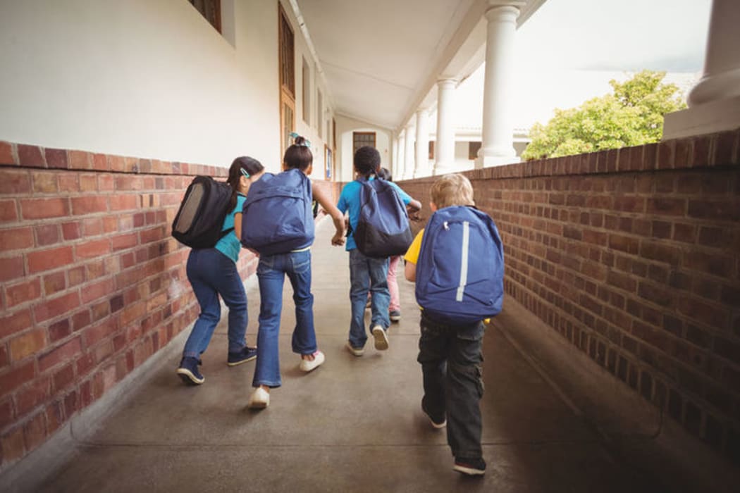 A photo of school kids with one trailing slightly behind