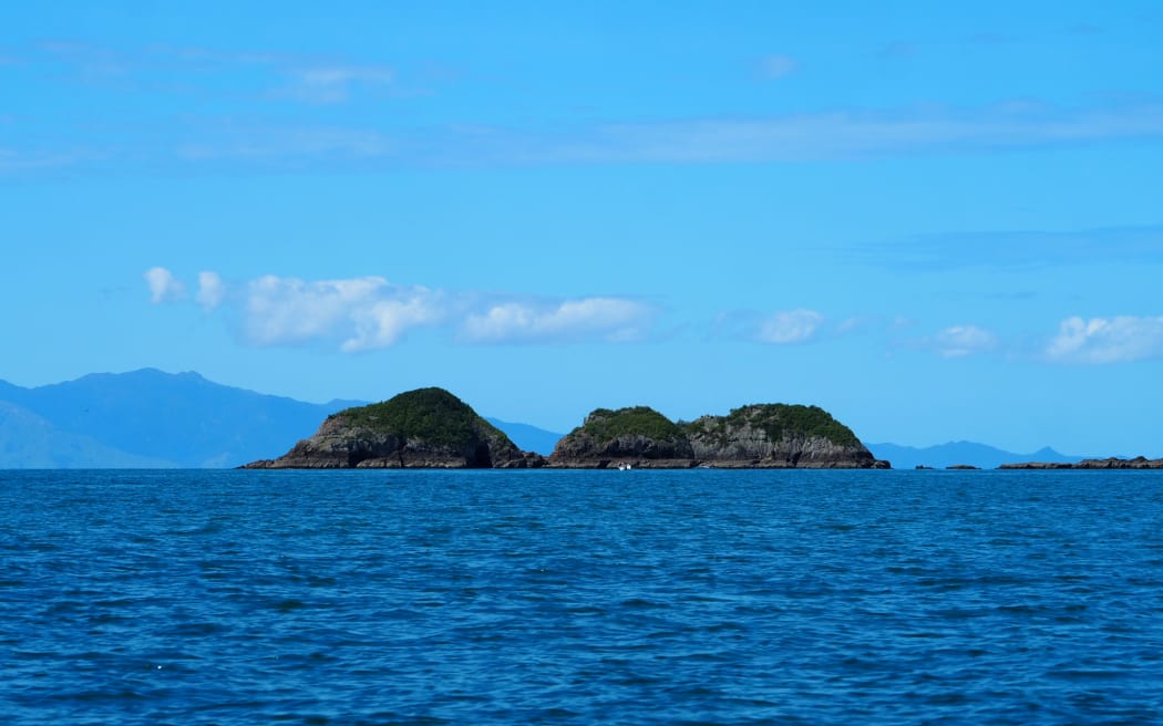 Small rocky islands on the horizon beneath a blue sky and above a blue sea.