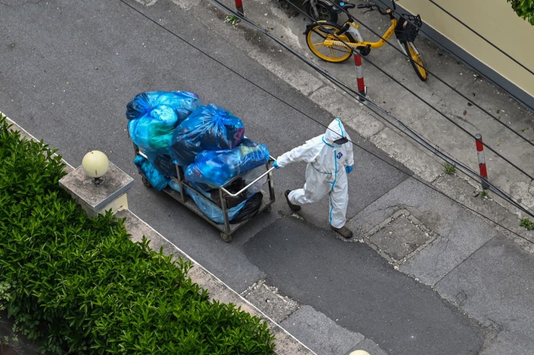 A worker in Shanghai wears PPE, and pulls along a cart filled with trash.