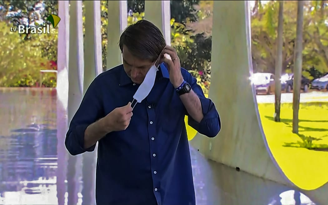 Screen grab from TV Brasil showing Brazilian President Jair Bolsonaro putting a face mask on as he prepares to speak with journalists at Planalto Palace in Brasilia on 7 July 2020.