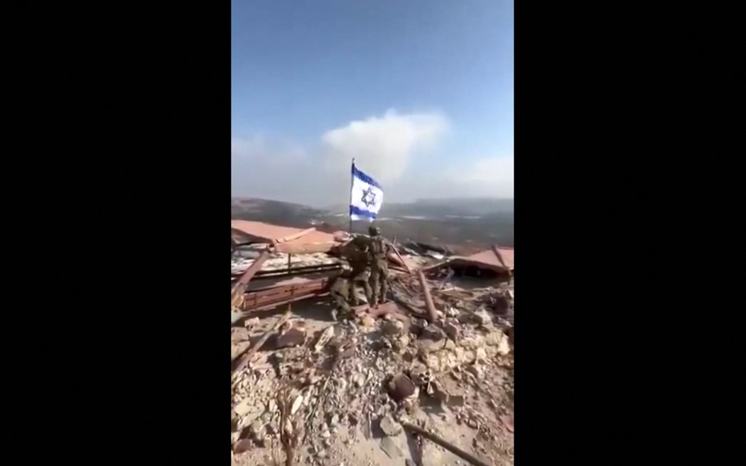 An image grab taken from a UGC video posted on social media on October 8, 2024 shows Israeli soldiers raising an Israeli flag in Lebanon's southern border village of Maroun al-Ras. - Hezbollah said it had forced Israeli troops to retreat on October 8 after they crossed into Lebanon near a UN peacekeeping (UNIFIL) post following Israel's announcement last week it was conducting ground incursions. (Photo by UGC / AFP) / NO USE AFTER OCTOBER 18, 2024 17:25:21 GMT - RESTRICTED TO EDITORIAL USE – MANDATORY CREDIT «  AFP PHOTO / UGC / ANONYMOUS  » - NO MARKETING NO ADVERTISING CAMPAIGNS – DISTRIBUTED AS A SERVICE TO CLIENTS [NO ARCHIVE]