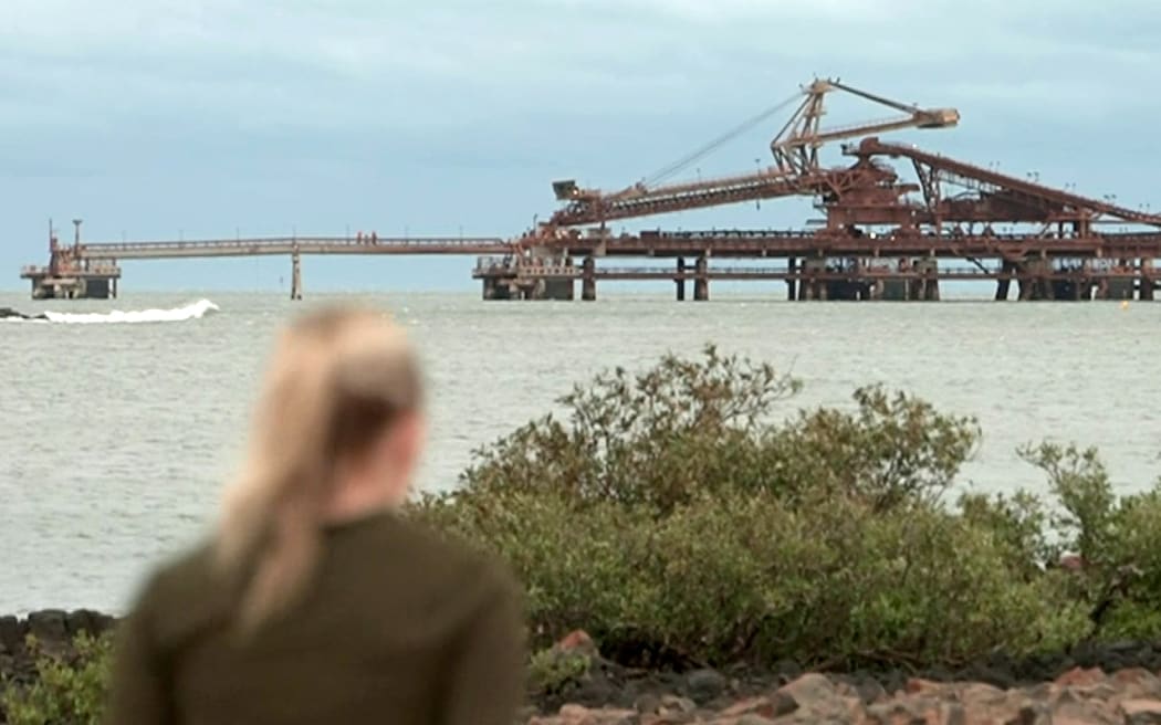 This frame grab taken from video footage provided by Australian Broadcast Corporation (ABC) on February 13, 2025 via AFPTV shows a local walking near wharfs that are part of mining operations at Port Hedland, ahead of the arrival of category five Cyclone Zelia. Forecasters said the slow-moving, severe tropical cyclone was moving south on February 13 morning towards Port Hedland -- one of the world's busiest iron ore loading ports -- with landfall expected in the afternoon. (Photo by Handout / ABC / AFP) / - Australia OUT / - AUSTRALIA OUT /  - AUSTRALIA OUT / RESTRICTED TO EDITORIAL USE - MANDATORY CREDIT "AFP PHOTO /  AUSTRALIAN BROADCASTING CORPORATION (ABC)" - NO MARKETING NO ADVERTISING CAMPAIGNS - DISTRIBUTED AS A SERVICE TO CLIENTS
