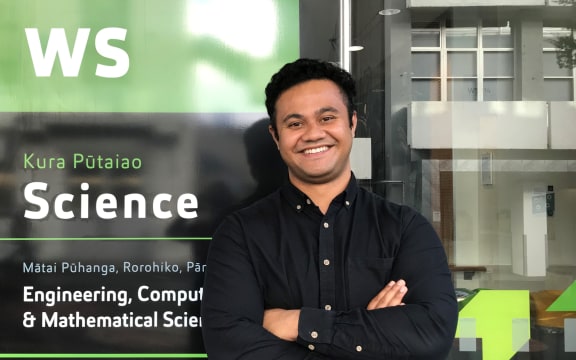 Dr Taniela Lolohea stands in front of the Science building on the AUT campus. He is smiling and has his arms folded.