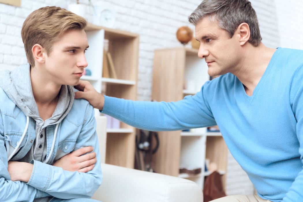 A photo of a father trying to talk to his son, and troubled teenager beginning to listen. Father reaches out with his hand.