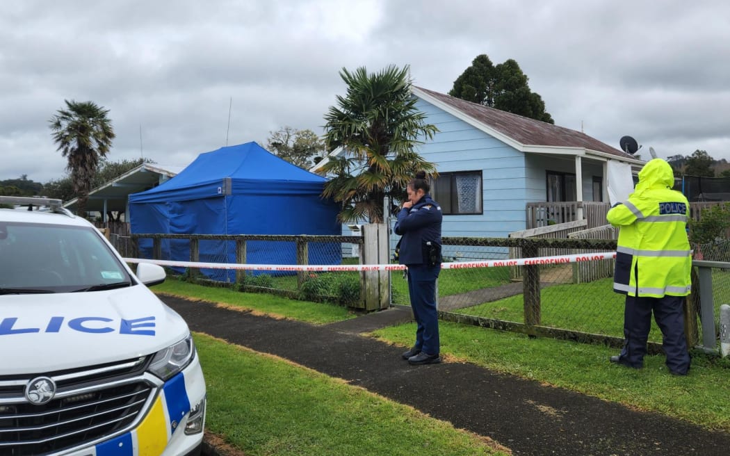 Police are executing a search warrant at a house on Taraire Street in relation to the investigation into the homicide of Linda Woods. At least four officers are guarding the cordoned house and other officers can be seen rummaging through rubbish bins on the property.