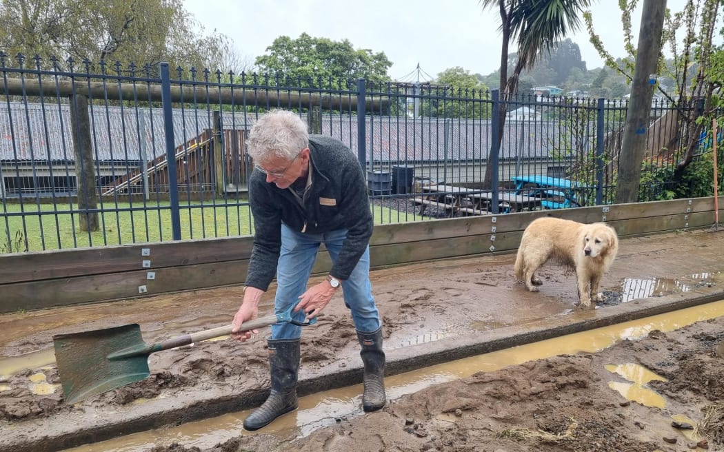 A Macandrew Bay resident helps to clear mud and debris from Conway Street behind the local school. He says a flood barrier helped to protect the school from damage.