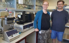 Erica Prentice and Vic Arcus in the lab, standing next to the machine they use to test enzyme reactions at different temperatures.