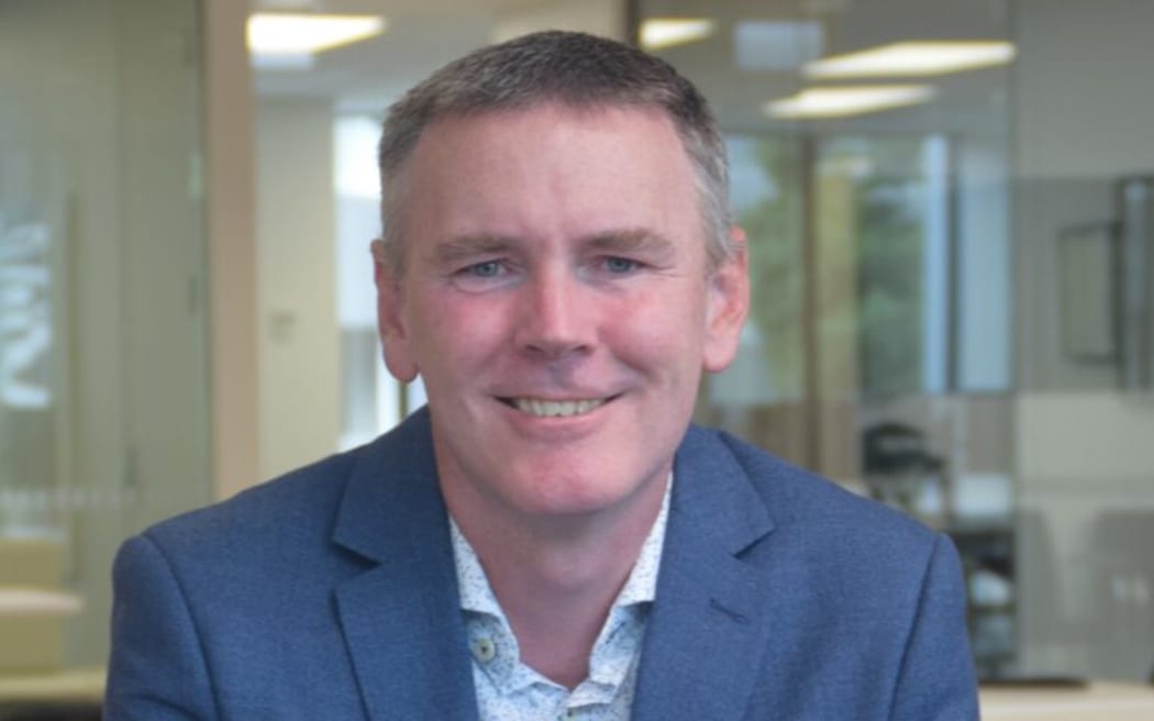 This is a head shot of Greame Ward. He is wearing a blue suit and sat in what looks like a meeting room.