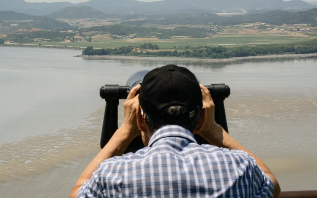 A visitor uses binoculars to watch the North Korean side of the Demilitarized Zone (DMZ) dividing the two Koreas, from South Korea's Odusan Unification Observatory in Paju on June 12, 2025. North Korea appears to have stopped broadcasting strange and unsettling noises along the border, Seoul's military said on June 12, a day after South Korea ceased blaring its own loudspeaker propaganda northwards. (Photo by ANTHONY WALLACE / AFP)