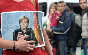 A refugee holds a picture of German Chancellor Angela Merkel after the arrival of refugees at the main train station in Munich, southern Germany, September 05, 2015.