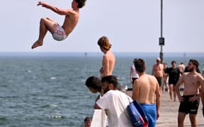 People jump off the Kerferd Road Pier as people cool off in heatwave conditions at Melbourne's Albert Park Beach on 22 November, 2024.