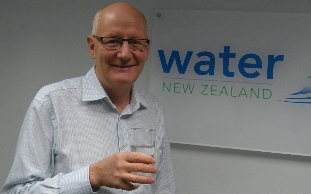 Man holds glass of water in front of  Water NZ sign