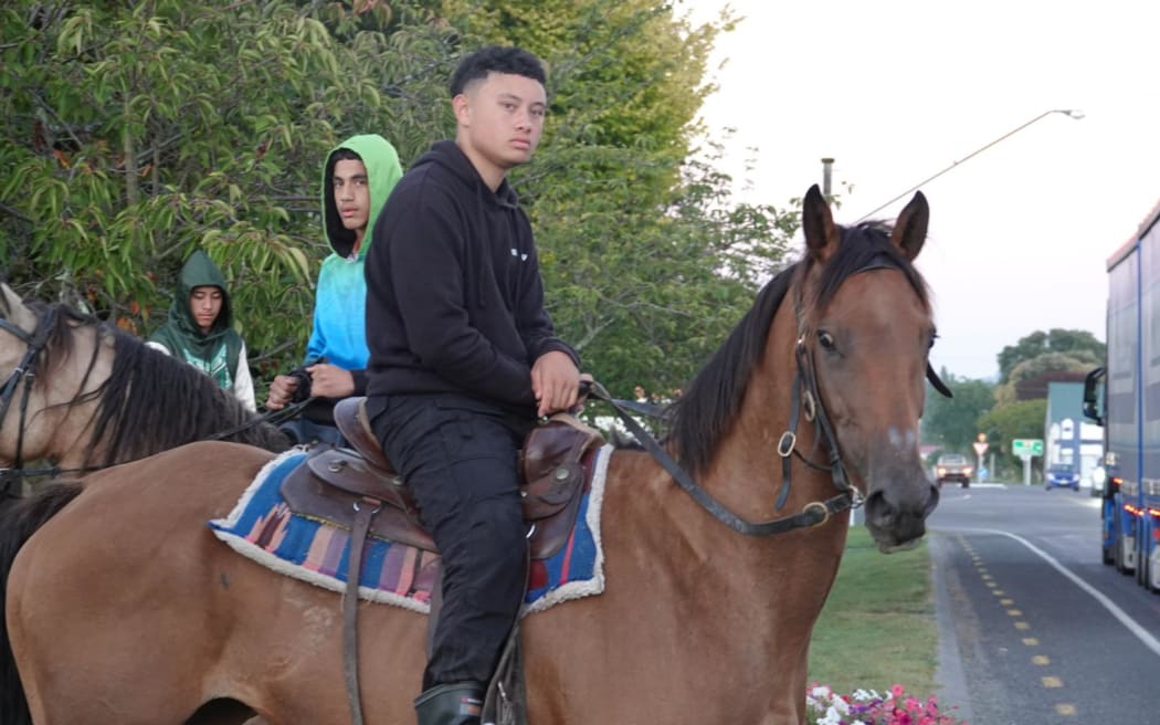 A young person wearing all black is sitting on a brown horse. There are two other young people on horses behind them.