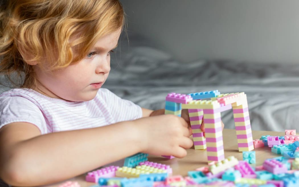 Little beautiful child playing with toy plastic building blocks, sitting at the table. Small girl busy with fun creative leisure activity. Development of fine motor skills for children.