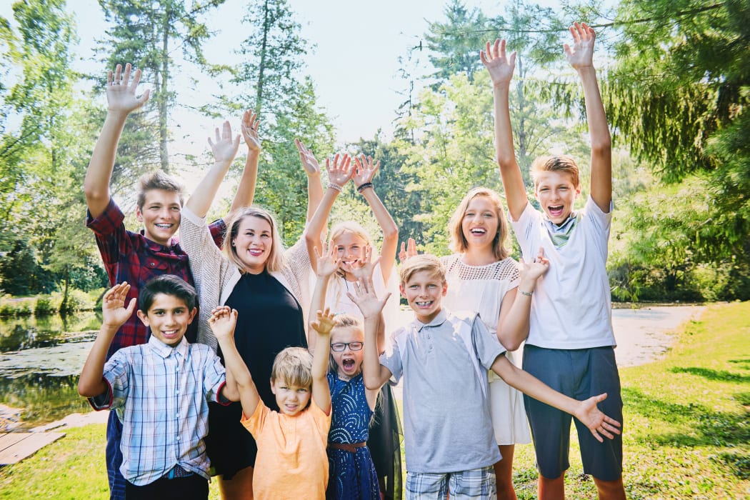 A photo of happy brothers and sisters  raising arms in the park