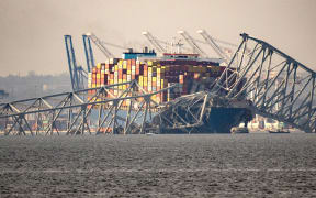 Part of the steel frame of the Francis Scott Key Bridge sits on top of the container ship Dali after the bridge collapsed in Baltimore, Maryland, on March 26, 2024. The bridge collapsed early March 26 after being struck by the Singapore-flagged Dali container ship, sending multiple vehicles and people plunging into the frigid harbor below. There was no immediate confirmation of the cause of the disaster, but Baltimore's Police Commissioner Richard Worley said there was "no indication" of terrorism. (Photo by Kent Nishimura / AFP)