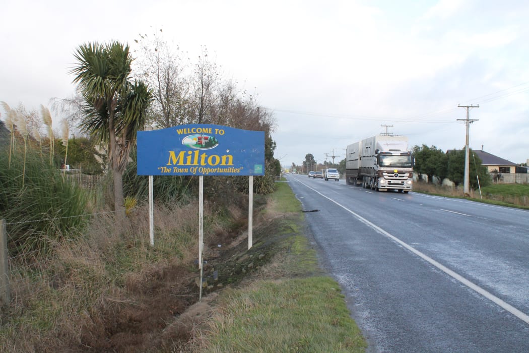 A photo of the road to Milton, showing the town sign and traffic.