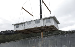 The first house being built by carpentry students at the prison has been completed, a crane lifted the building over the wire so it can be transferred to a permanent site.