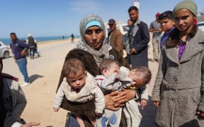A woman carries three babies as she reaches the central part of the Gaza Strip after fleeing the Al-Shifa hospital compound in Gaza City, on March 21, 2024. Israel's army was on March 21 four days into a raid at Al-Shifa, Gaza's largest hospital, where the military says Hamas was operating from among patients and displaced civilians. (Photo by AFP)